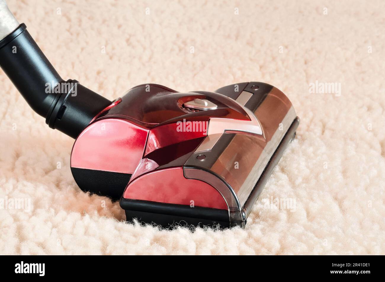 Home cleaning concept with vacuum cleaner. Close up of the head of a modern hoover being used while vacuuming a woollen furry carpet. Stock Photo