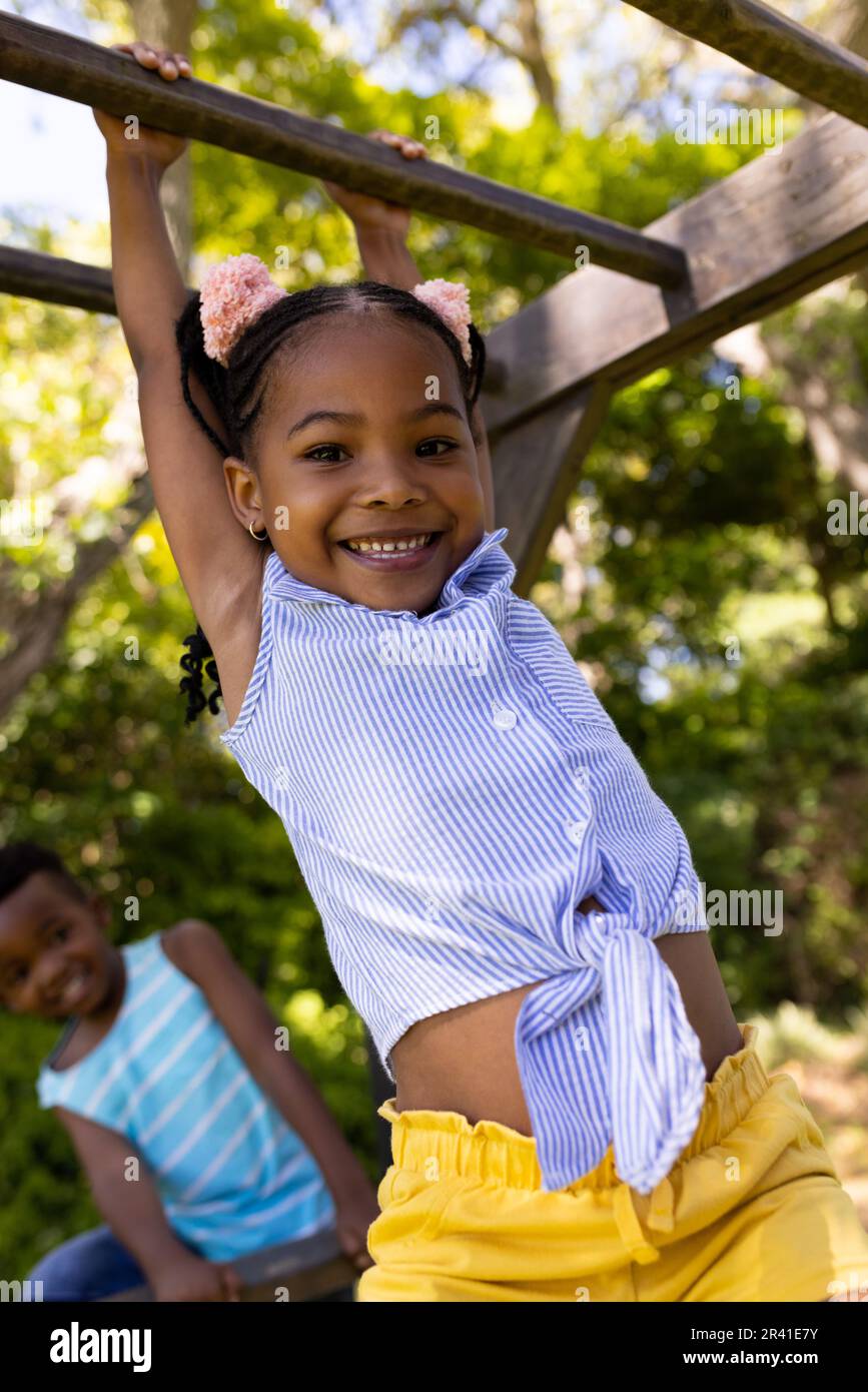 Low angle view of african american cute smiling girl hanging on monkeys bars at playground Stock Photo