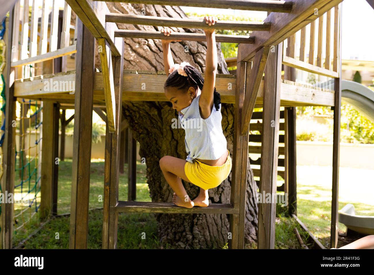 African american girl hanging on wooden monkey bars while playing in playground Stock Photo