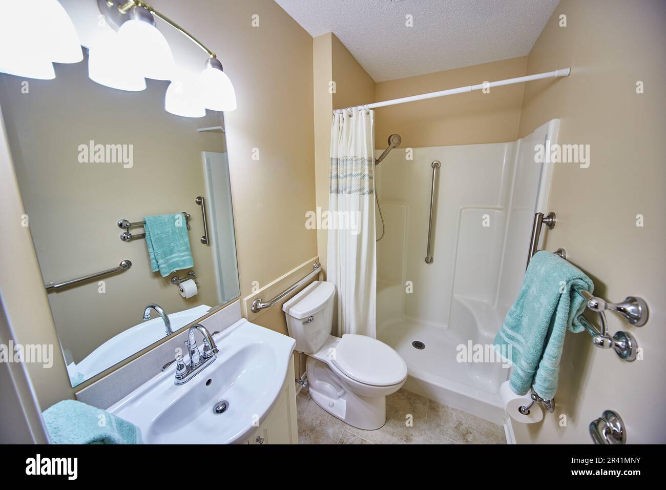 Clean white and beige handicap bathroom with built in railing and shower seating teal blue towel