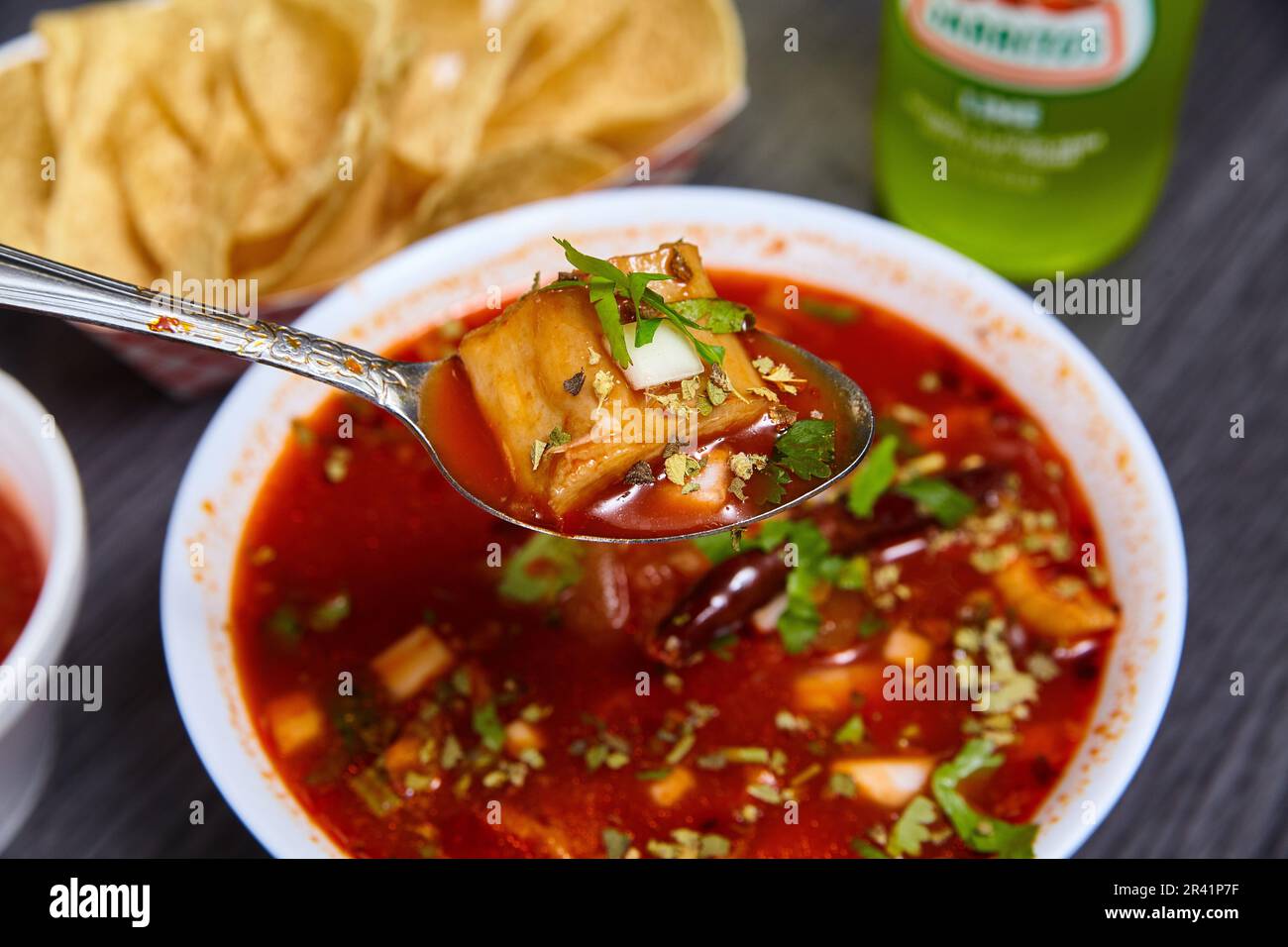 Menudo soup hominy grits tripe stew Mexican meal Jarritos lime soda tortilla chips food in spoon Stock Photo