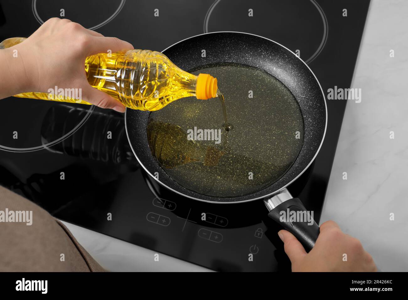 https://c8.alamy.com/comp/2R426KC/woman-pouring-cooking-oil-from-bottle-into-frying-pan-on-stove-above-view-2R426KC.jpg