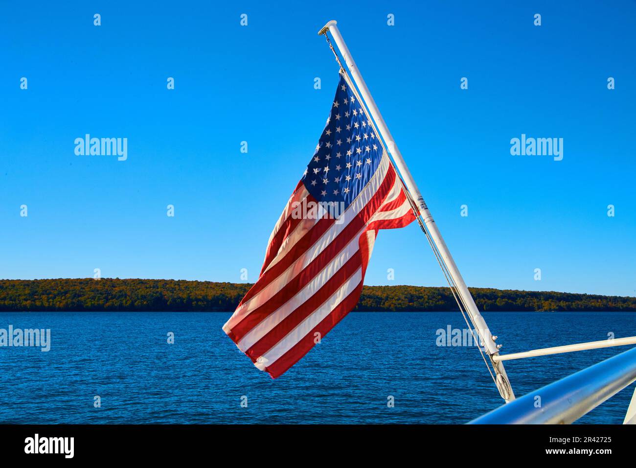 American flag hanging off boat with distant shore and calm lake or river waters Stock Photo