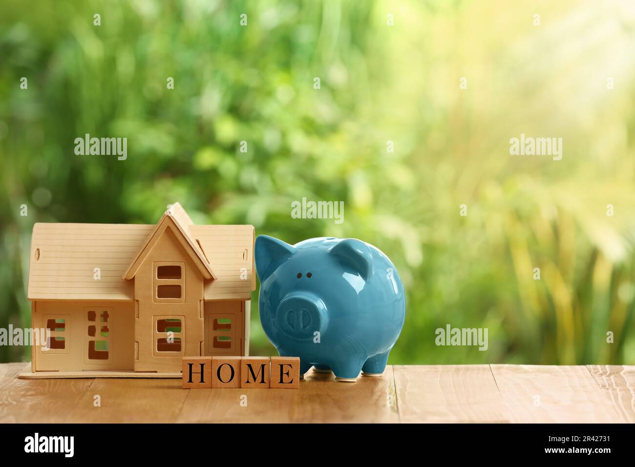 Piggy bank, house model and word Home made of cubes on wooden table outdoors. Space for text Stock Photo