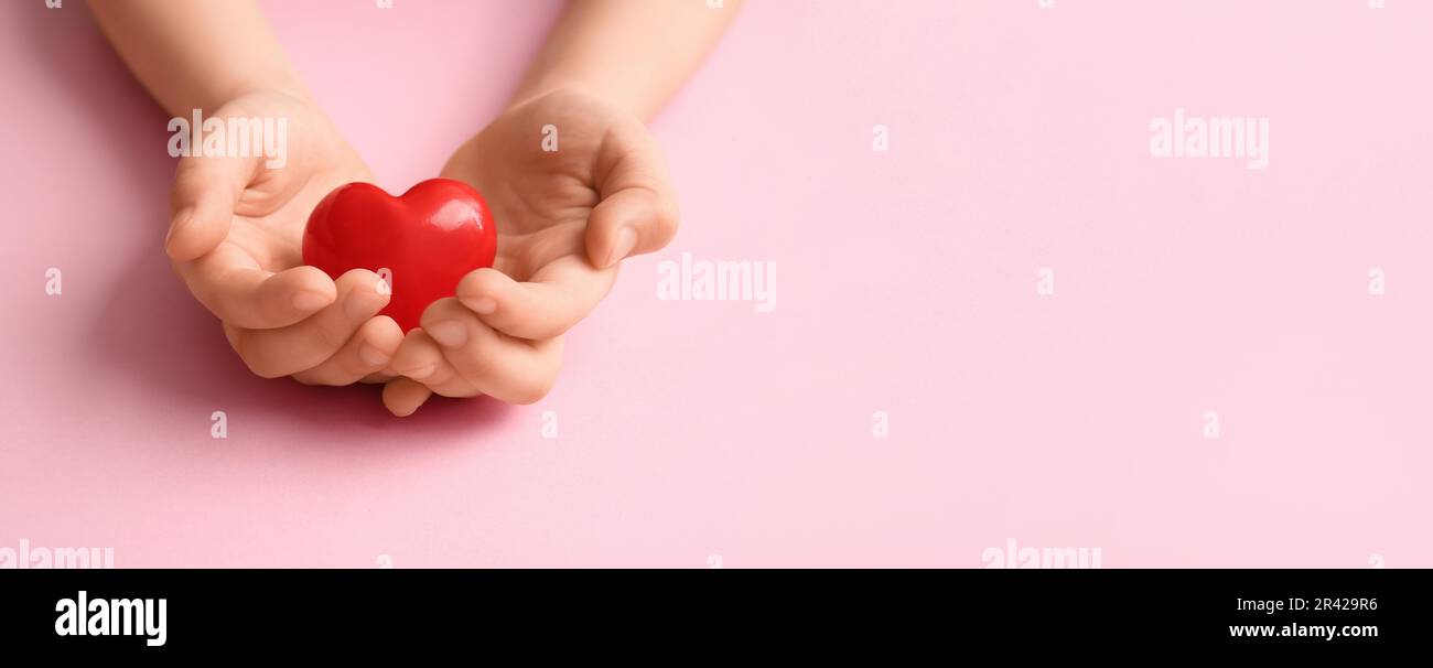 Child's hands with red heart on pink background with space for text ...