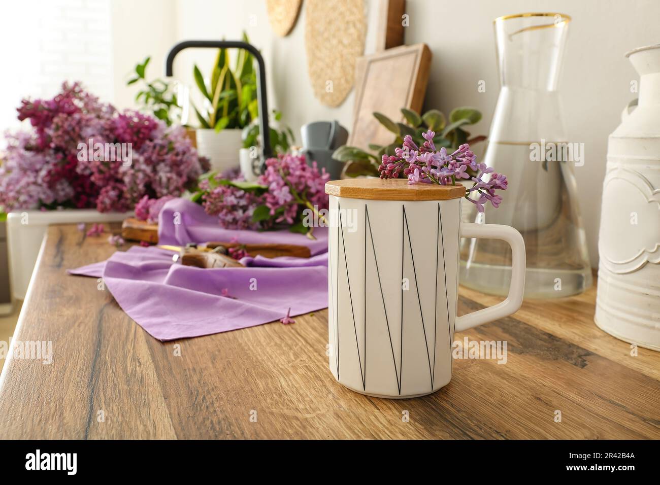 Cup with small twig of lilacs on kitchen counter Stock Photo