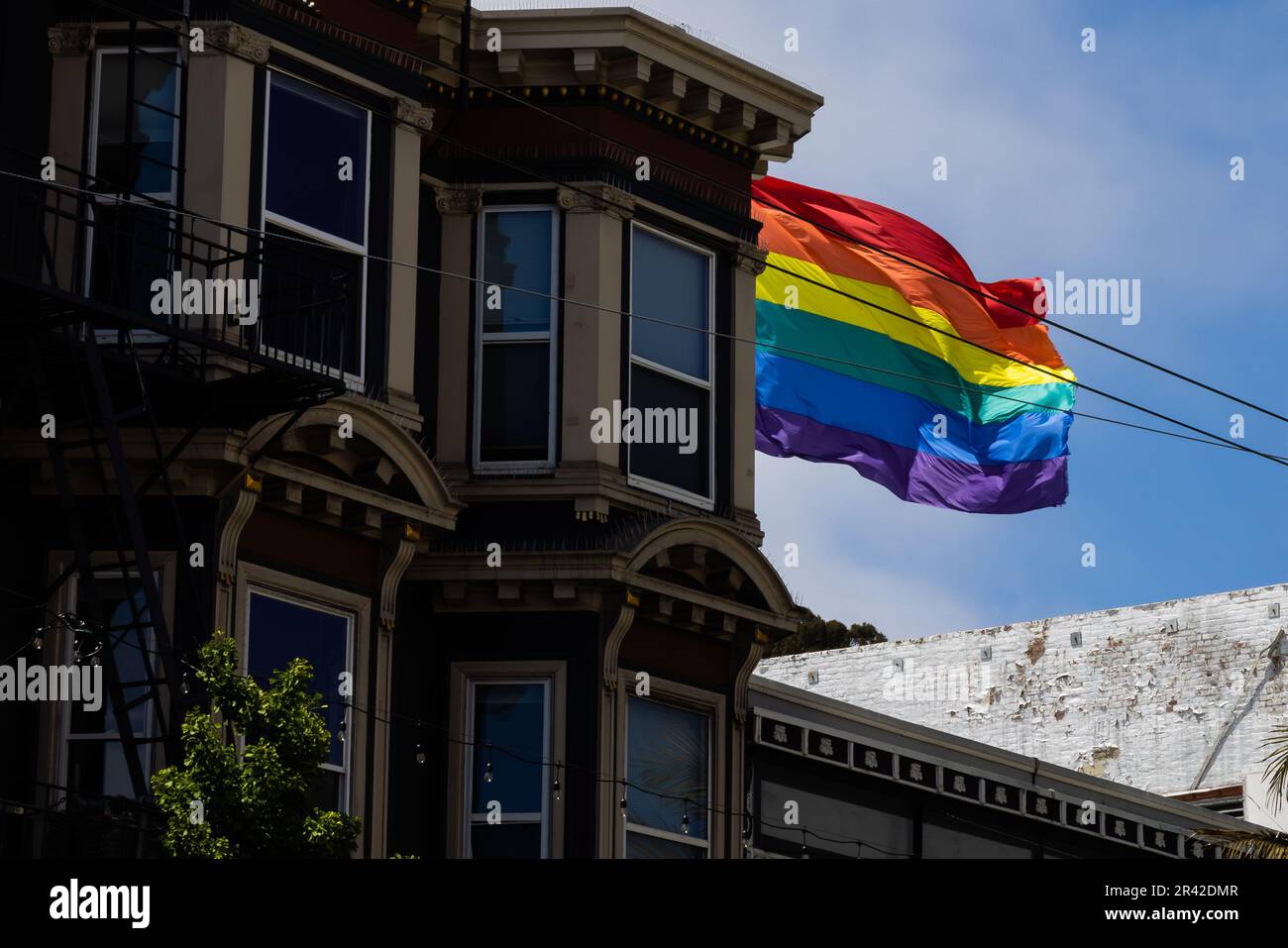 A stunning, multi-colored building stands proudly in the urban area with its rainbow flag flying high against a bright blue sky. The Castro District, Stock Photo