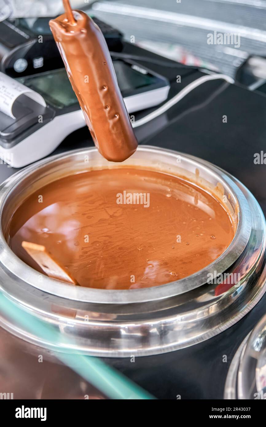 Salesman wearing plastic gloves dips ice cream on stick into hot chocolate. Process of popsicle