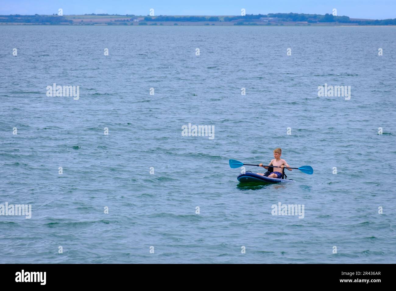 Young boy holds paddle in a kayak in the ocean at Whitstable Beach