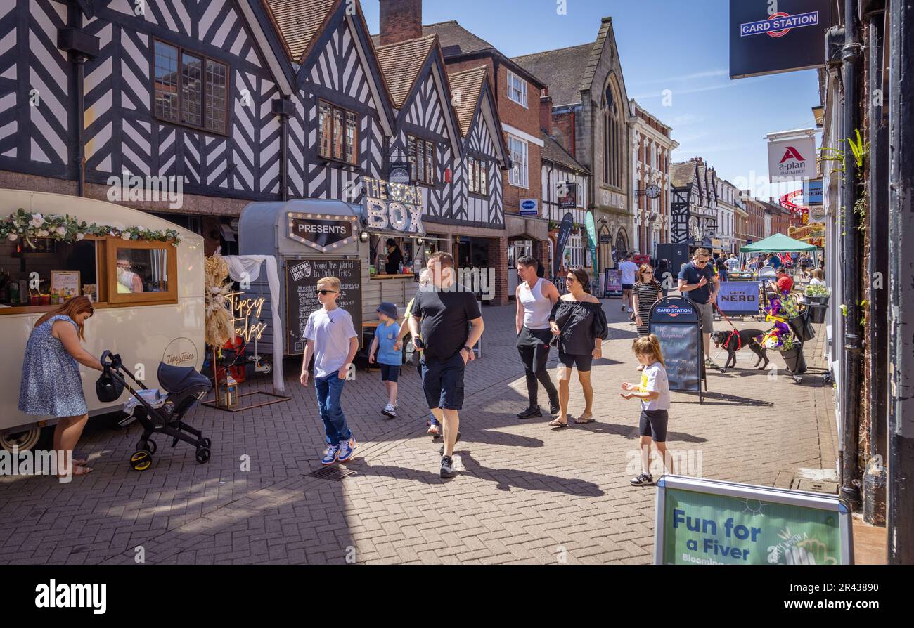 People enjoying the sun while walking along a busy street lined with shops and pop up food and drink stalls during Lichfield Food Festival. Stock Photo