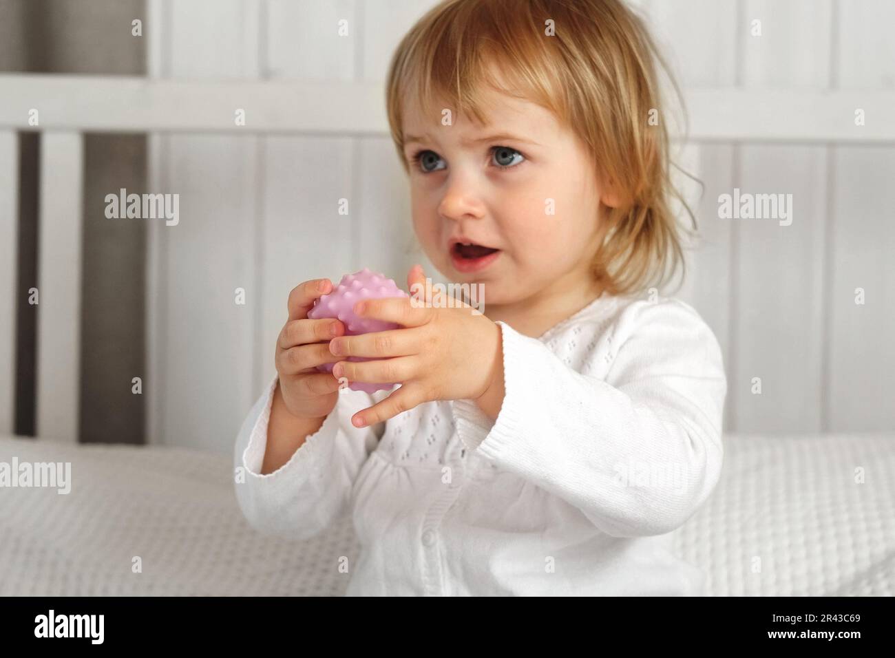 Cute baby girl playing tactile knobby balls. Young child hand plays sensory massage ball. Enhance the cognitive, physical process. Brain development. Stock Photo