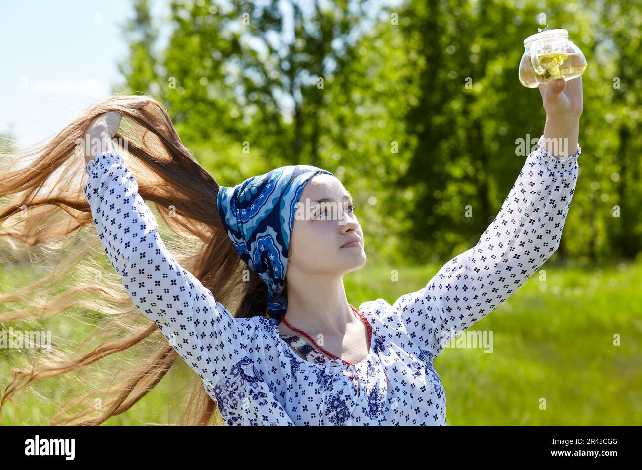 Woman holding transparent teapot with herbal tea. Collects fresh green herbs harvest and make healthy tea. Blurred image, selective focus Stock Photo