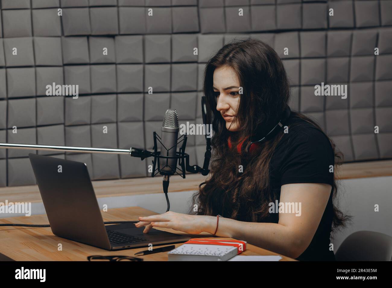 Young woman in the sound studio is record her voice on professional microphone. Online radio and podcasting concept. Stock Photo