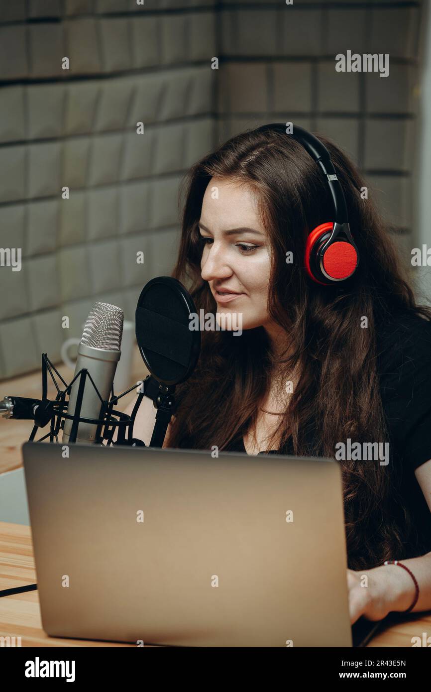 Young woman in the sound studio is record her voice on professional microphone. Online radio and podcasting concept. Stock Photo