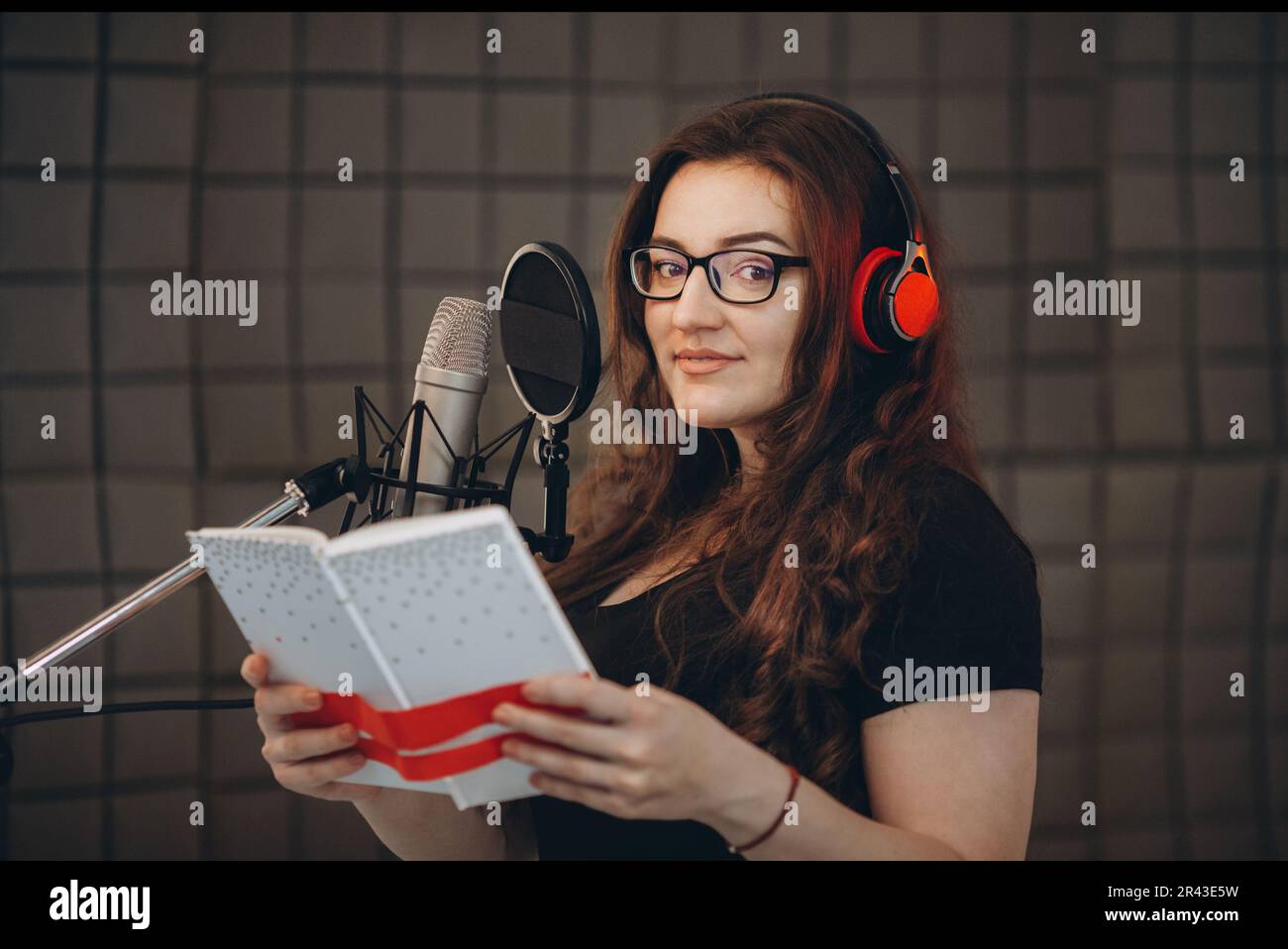 Professional female voice artist with headphones talking on mic during dubbing or voiceover. Online radio and podcasting concept. Stock Photo