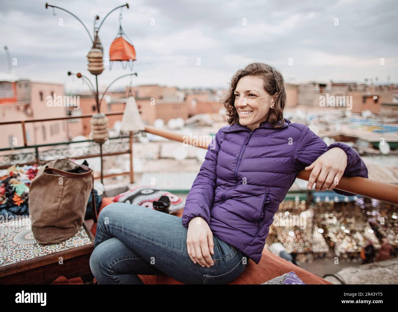 A young woman smiles while sitting on a rooftop in Marrakesh, Morocco Stock Photo
