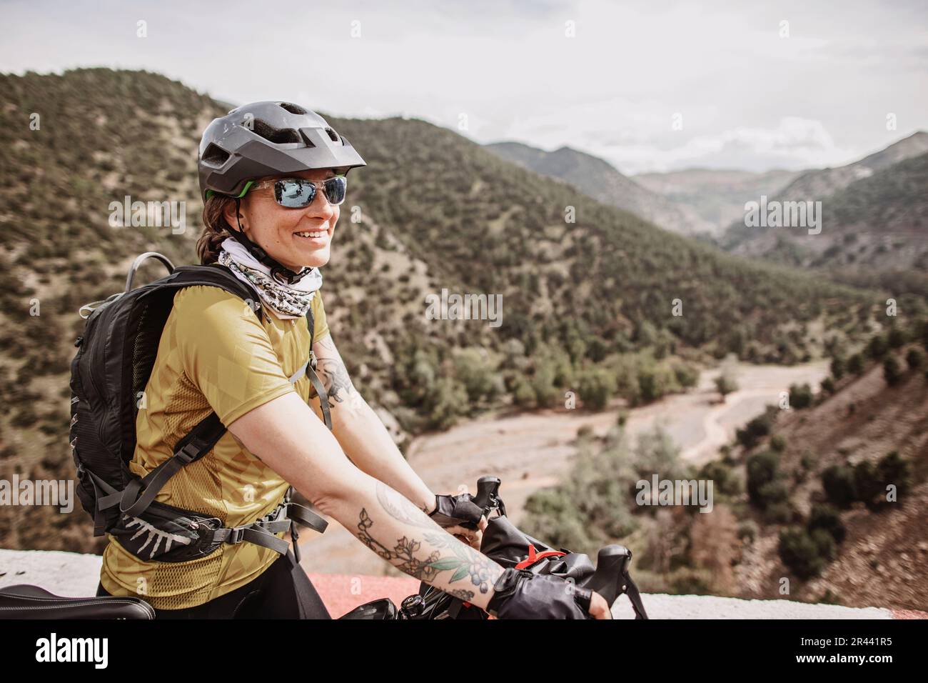 Female cyclist smiles while biking thru the Atlas Mountains, Morocco Stock Photo