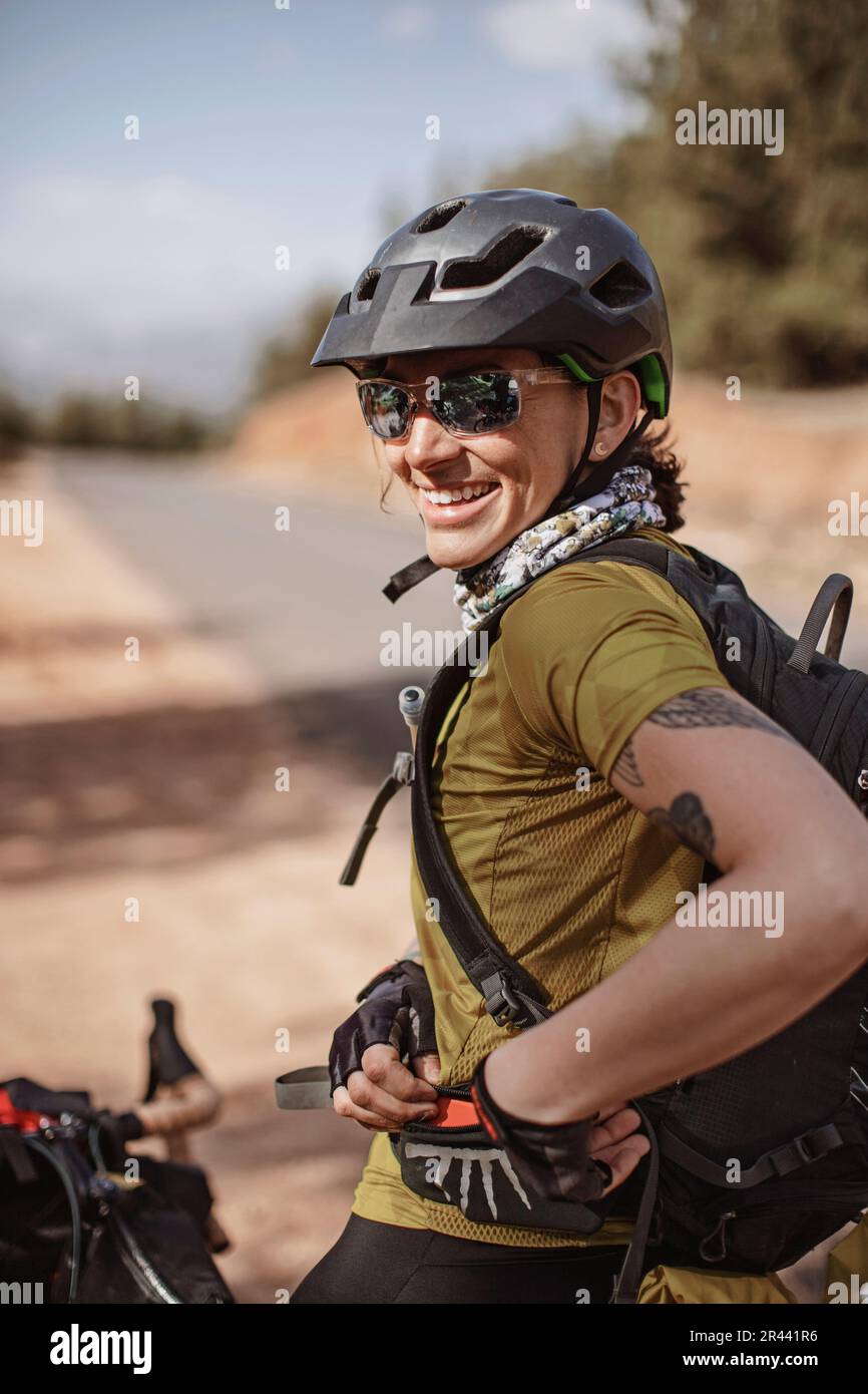 A female cyclist wearing sunglasses smiles while stopped on the road Stock Photo