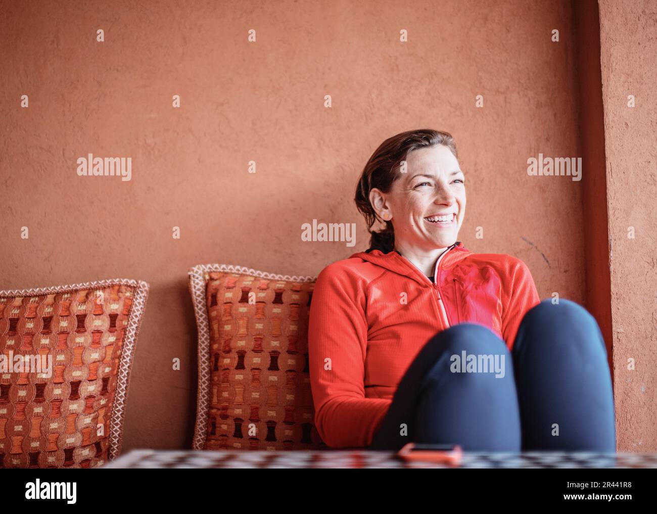 A smiling woman relaxes on  a couch next to an adobe wall in Morocco Stock Photo