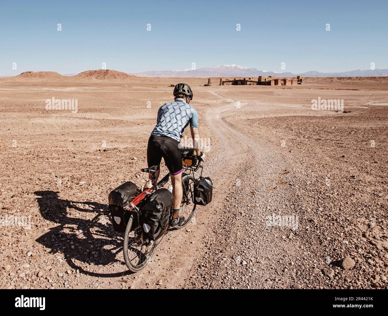 A cyclist rides through a desert toward ruins, Ouarzazate, Morocco Stock Photo