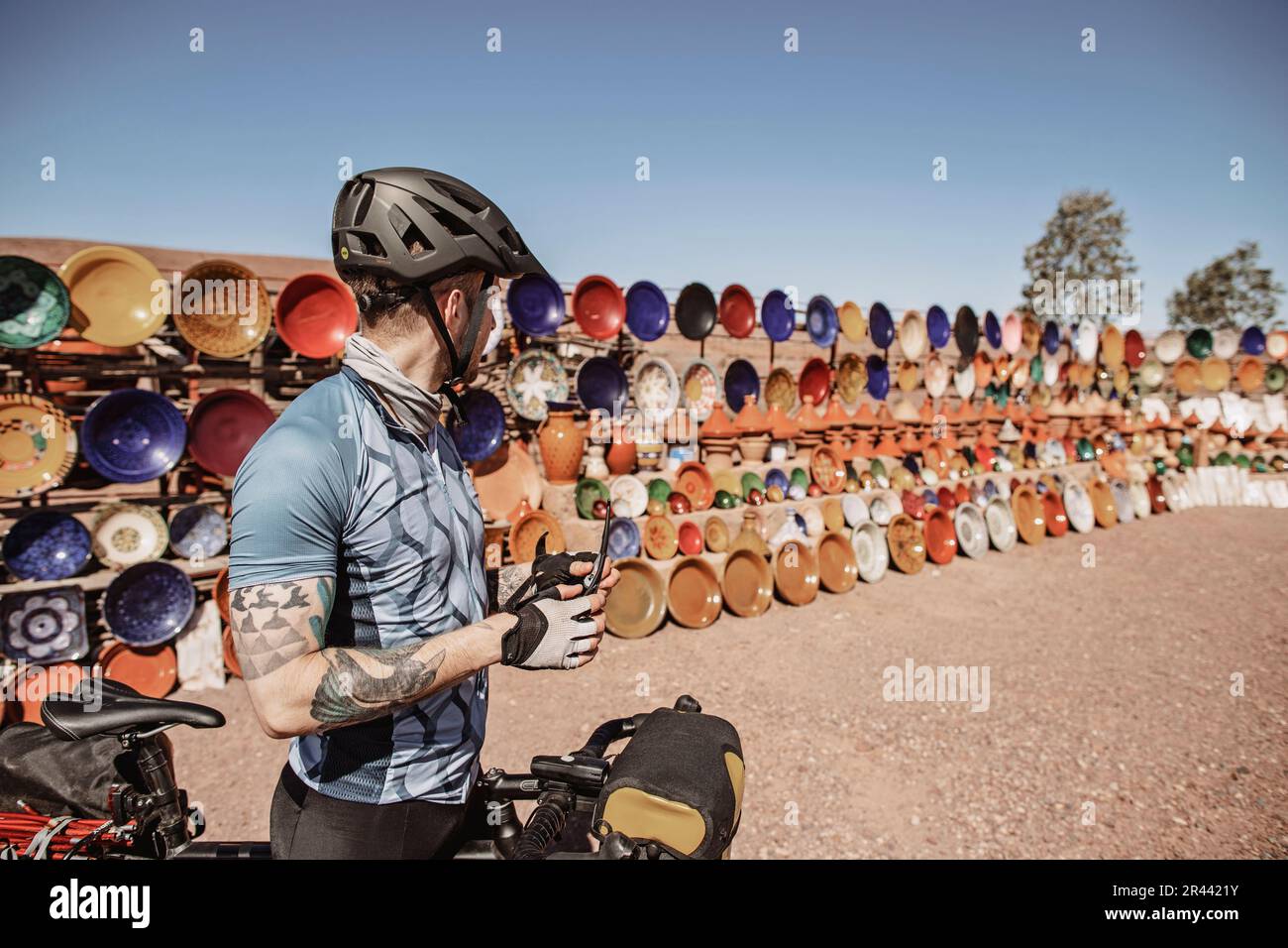 A male cyclist stops next to an outdoor ceramic market, Morocco Stock Photo