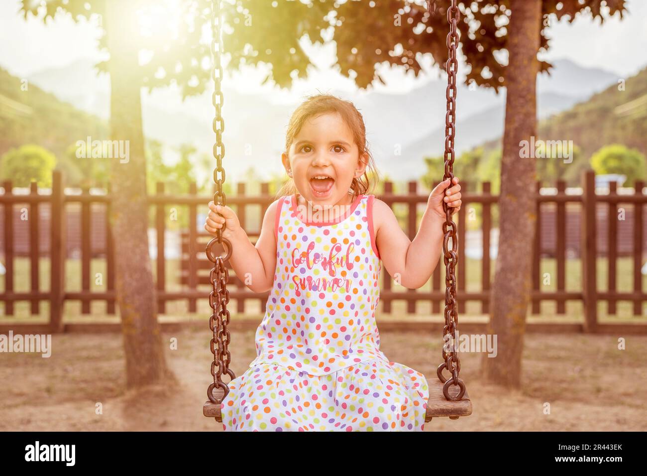 Happy girl sitting on a swing in the park. Stock Photo