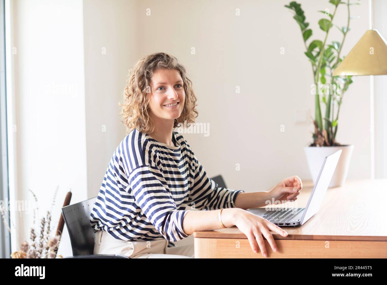 young woman sitting on a table in home office with laptop Stock Photo