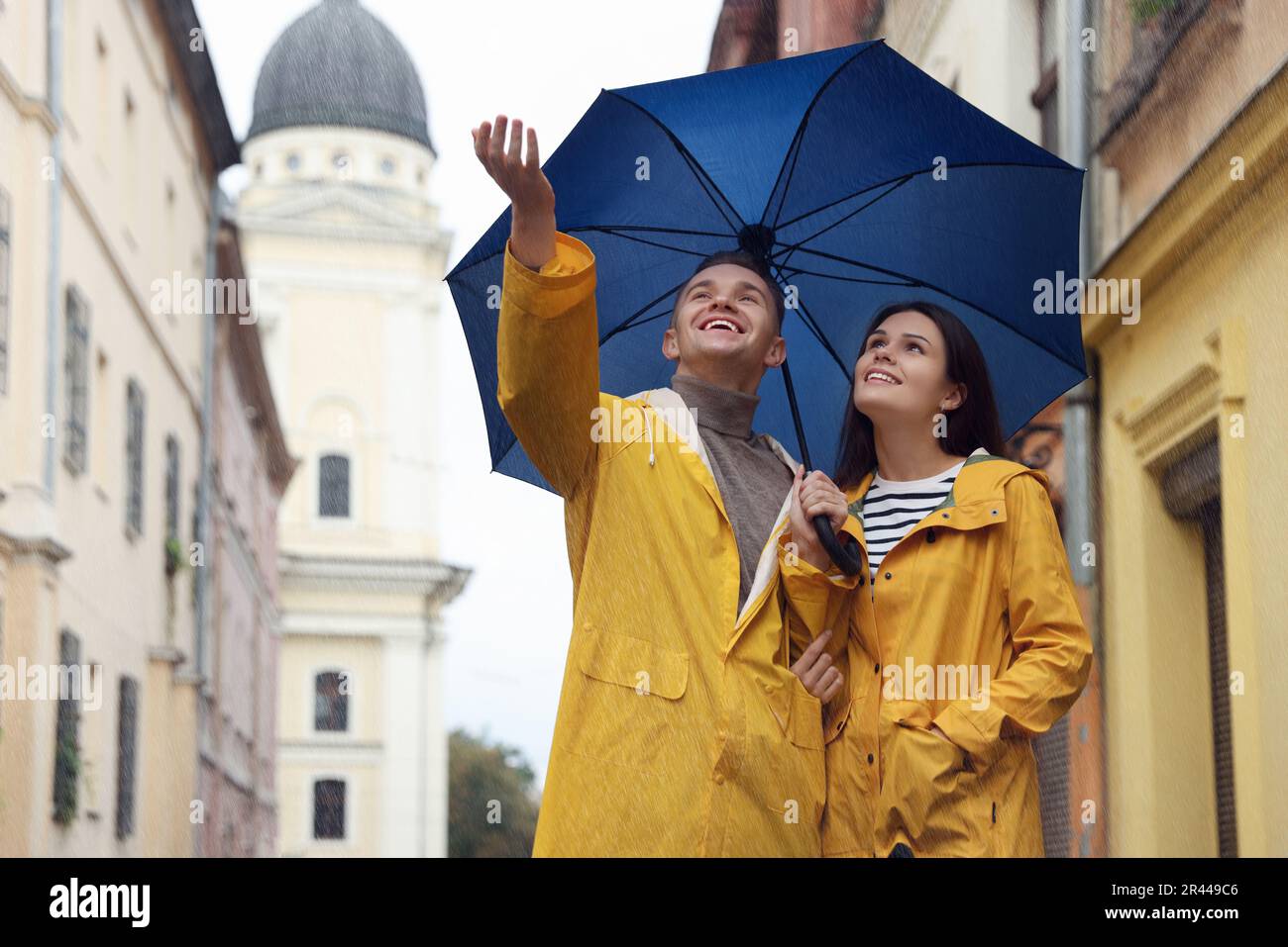 Lovely young couple with umbrella walking under rain on city street ...