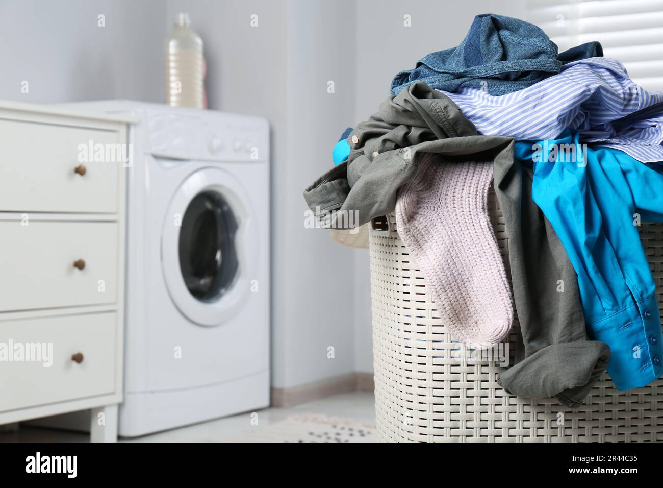 Plastic laundry basket overfilled with clothes in bathroom, closeup