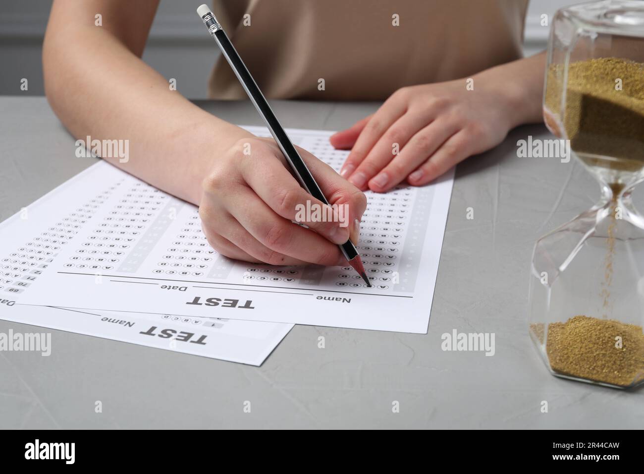 Student filling answer sheet at light grey table, closeup. Passing exam ...