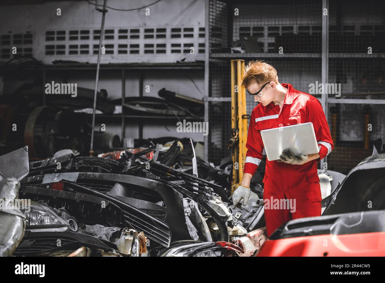 Old used car part warehouse worker checking inventory in garage. Staff worker working in recycle motor junkyard auto parts management. Stock Photo