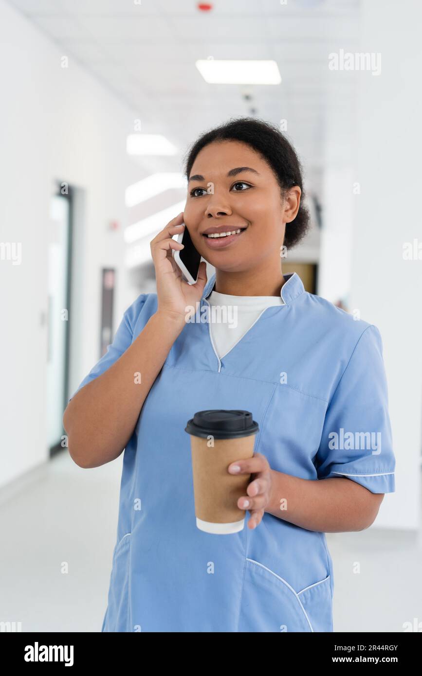 positive multiracial nurse smiling during conversation on smartphone