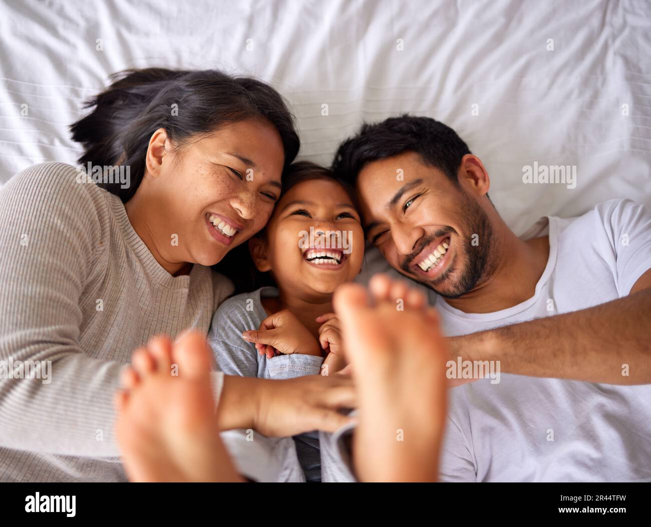 Fun, bed and happy family playing, wake up and happy from above, tickle and laughing in their home. Bedroom, games and girl with parents, smile and Stock Photo