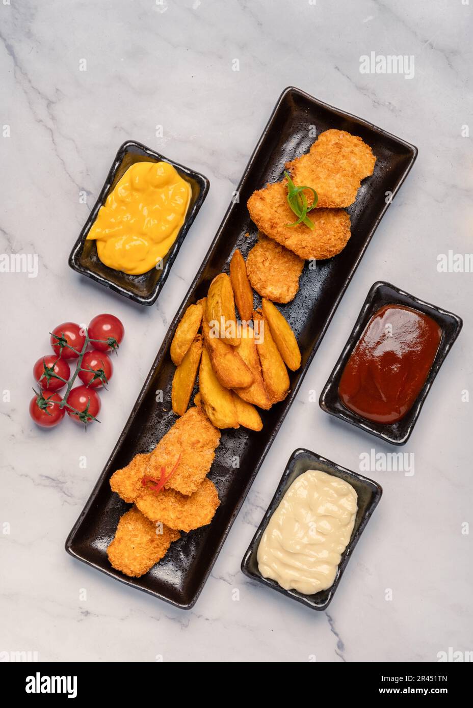 A top view of a platter of fried meat and potatoes near bowls of condiments Stock Photo