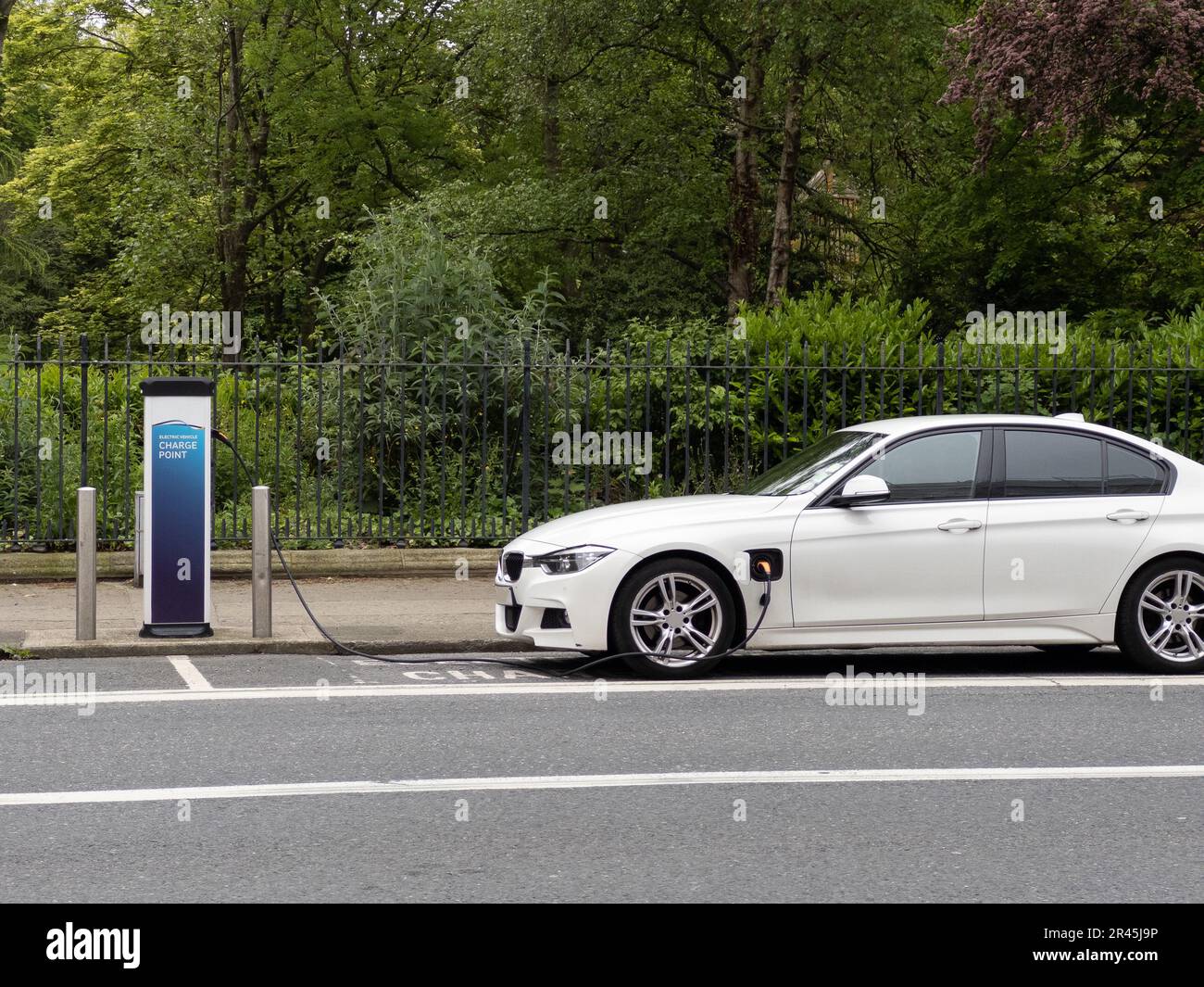 White electrical vehicle plugged into public outdoor charging station