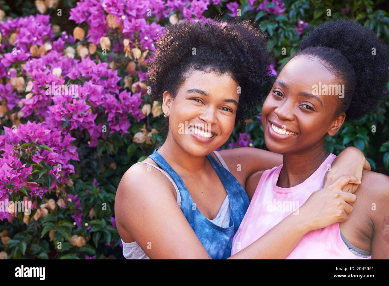 Two best friends hugging and posing outside in summer, pink flowers