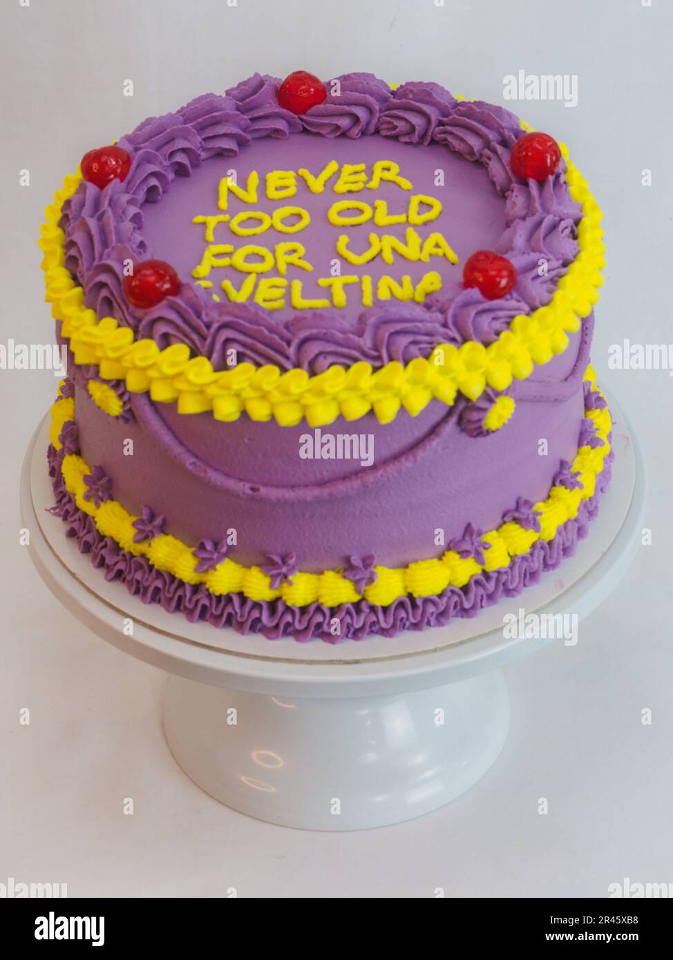 frosted icing violet yellow classic cilyndrical cake with text messagge topping on studio white background. Romantic layered cupcake. Stock Photo