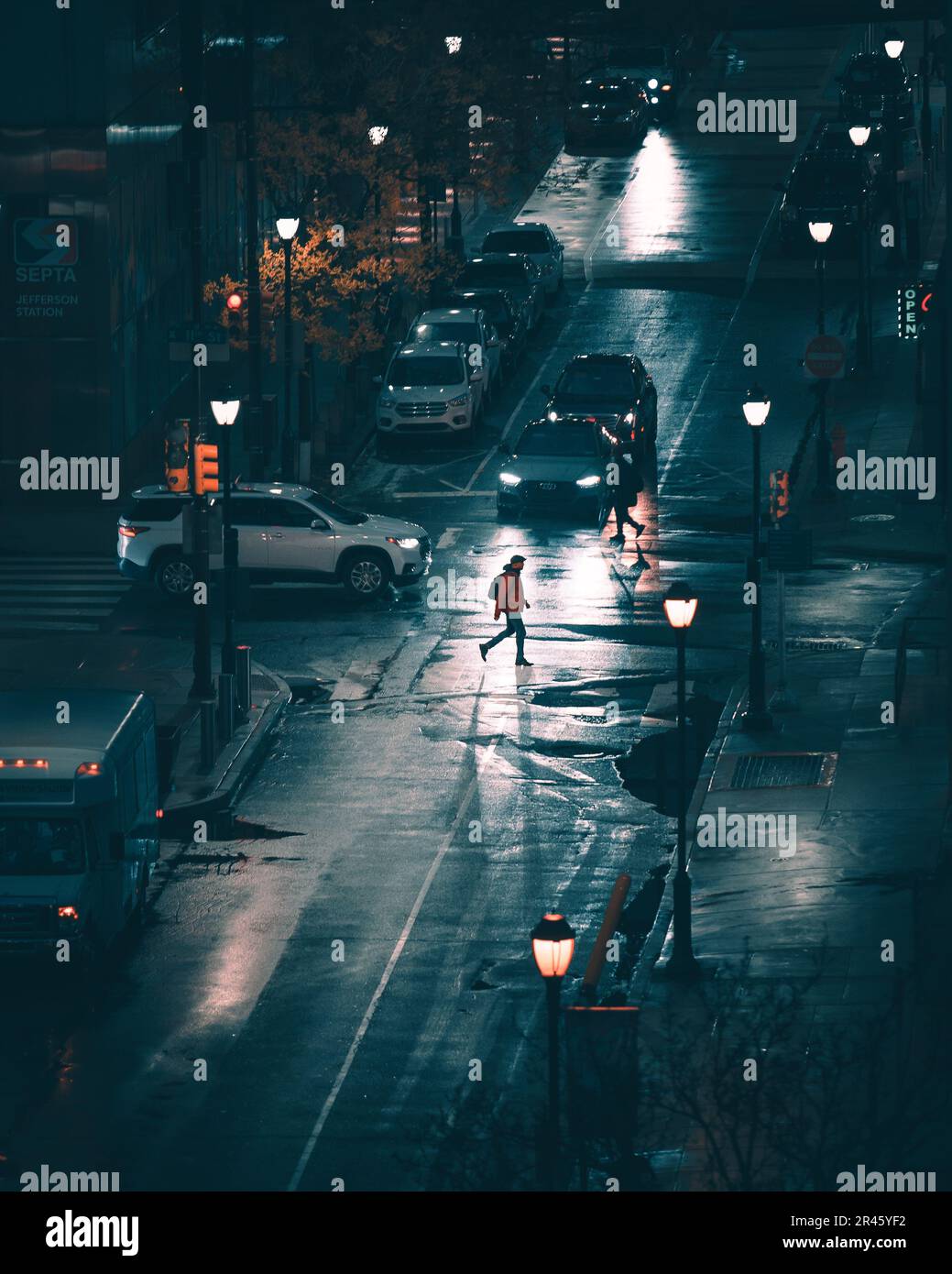 A lone figure strides down a city street illuminated by street lamps ...