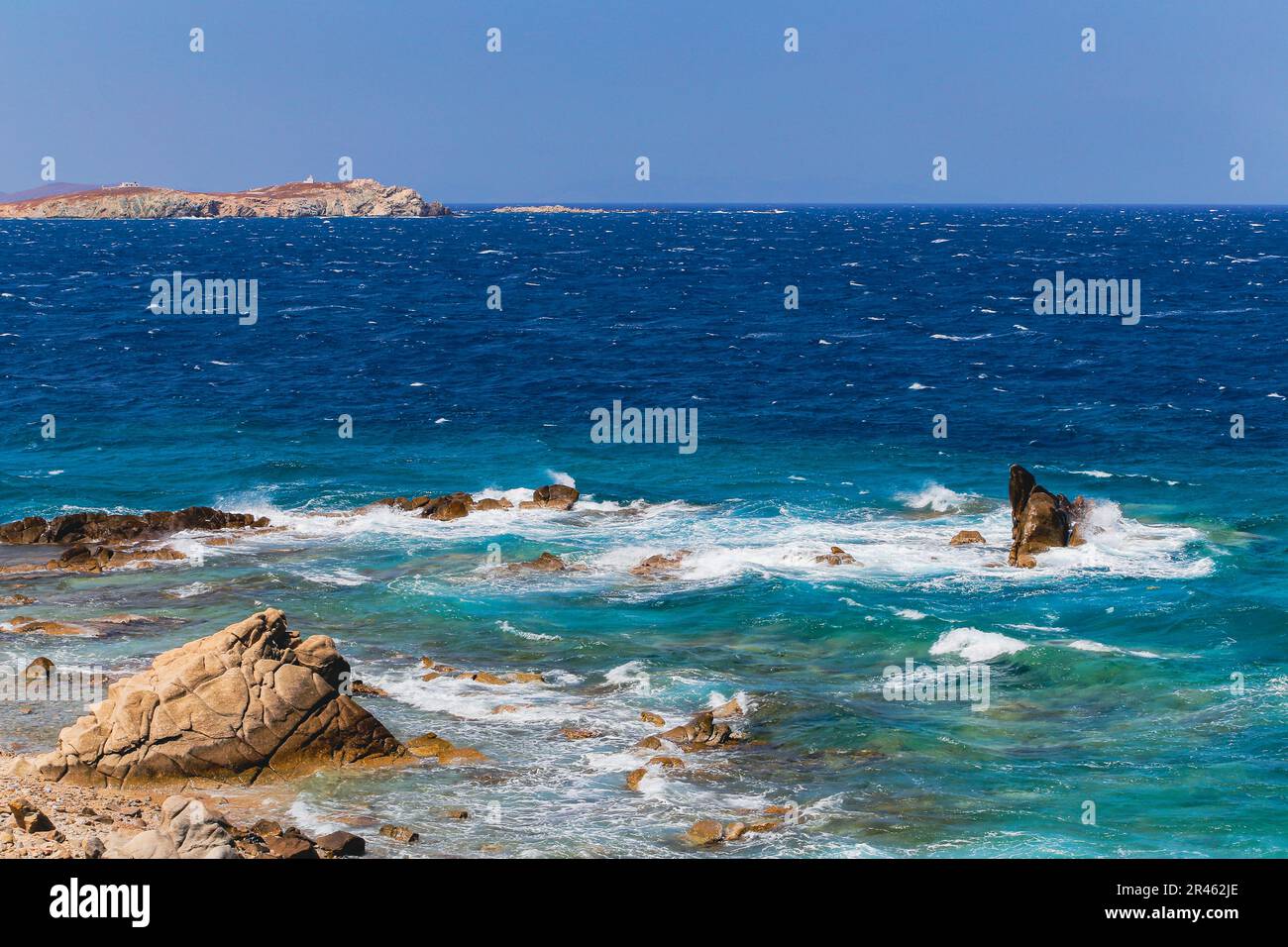 The blue sky over the sea with waves crashing on the rocks in Mykonos, Greece Stock Photo