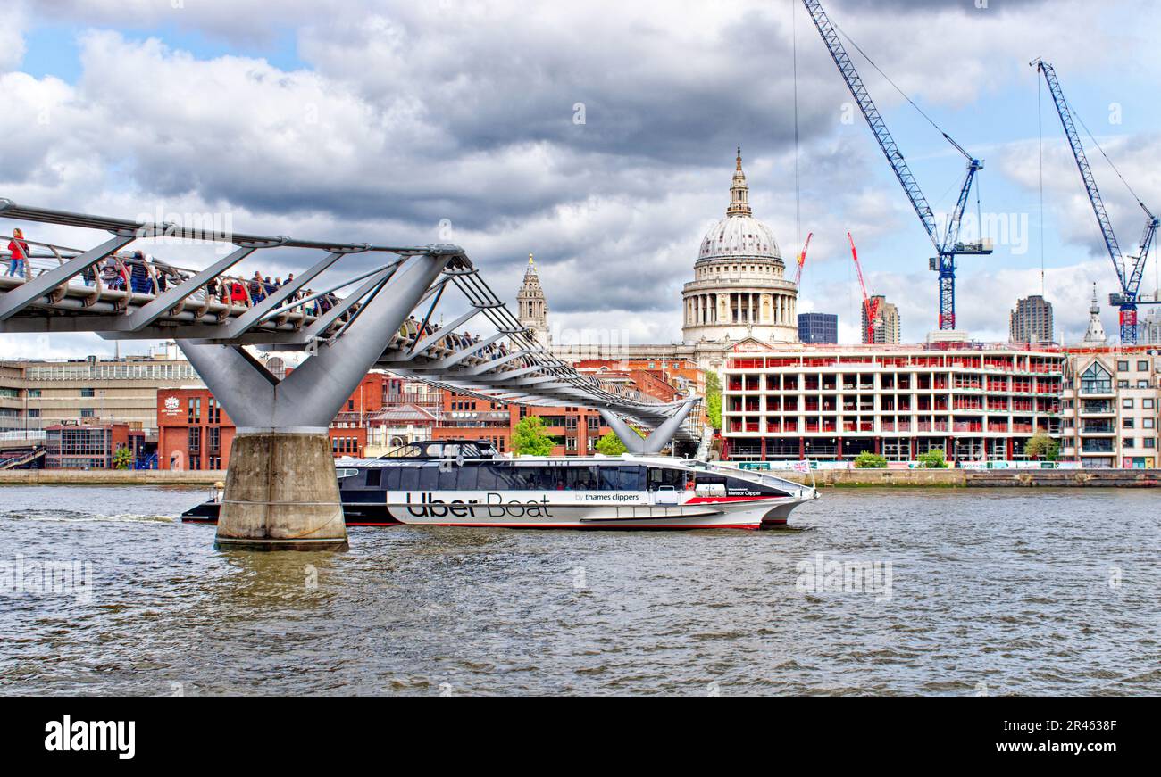 London the Millennium Footbridge over the river Thames leading towards St Pauls Cathedral and Uber boat passing under the bridge Stock Photo