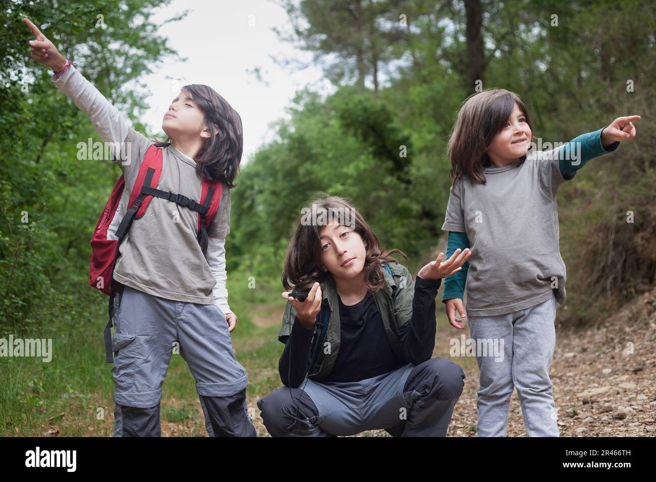 Two young siblings point in different directions, while their older brother wears an expression of uncertainty. Stock Photo