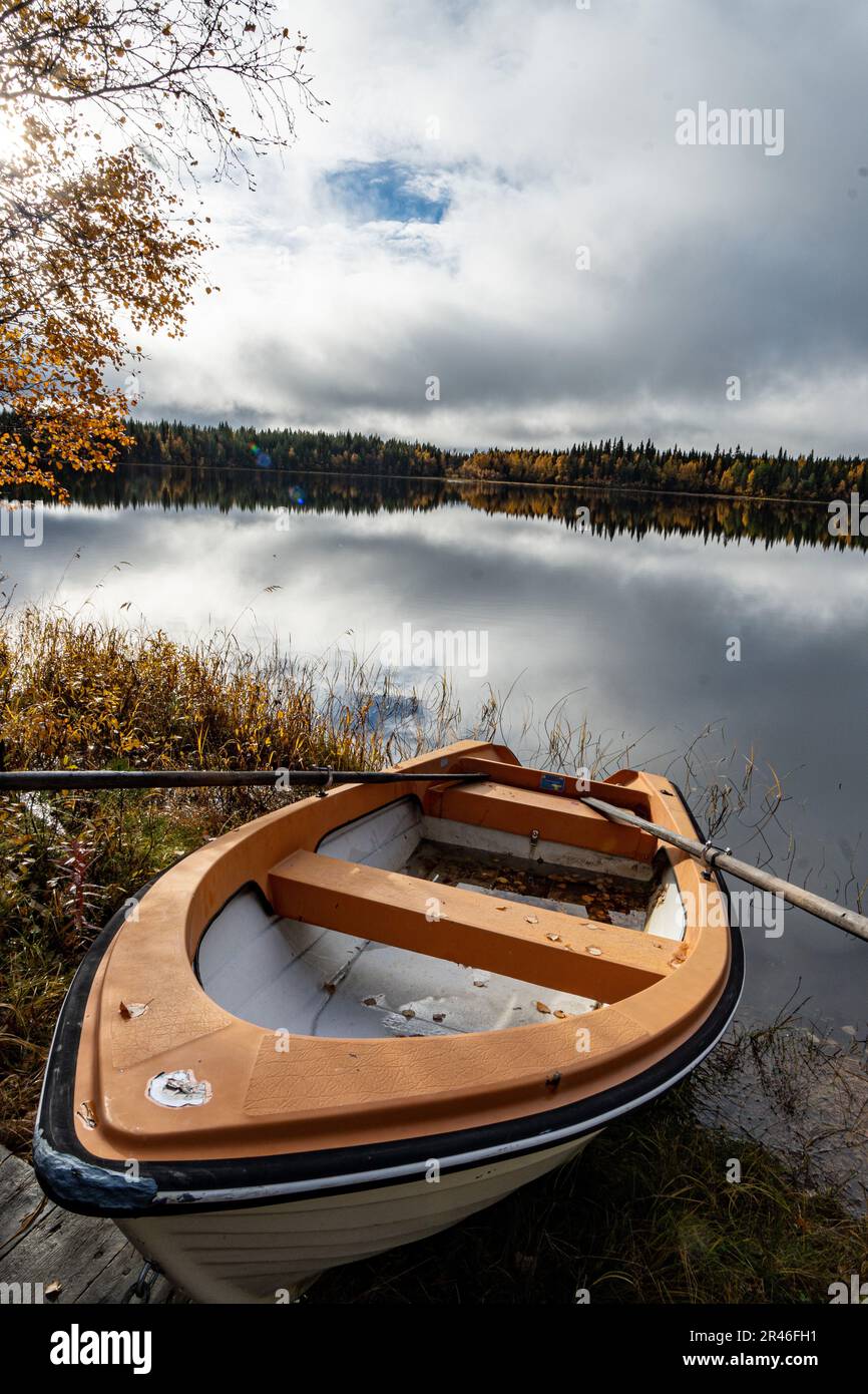 A boat is perched on the water's edge of a tranquil lake surrounded by golden autumn foliage Stock Photo