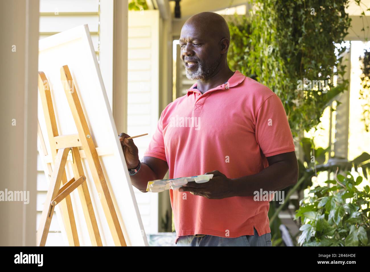 Happy senior african american man holding paint palette painting canvas on easel at home Stock Photo