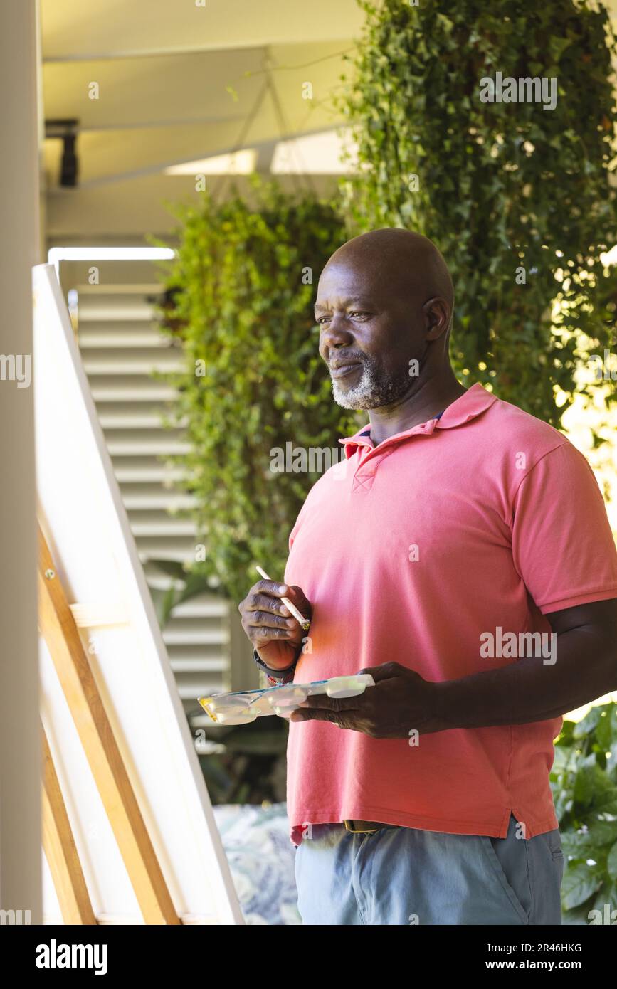 Happy senior african american man holding paint palette painting canvas on easel, copy space Stock Photo