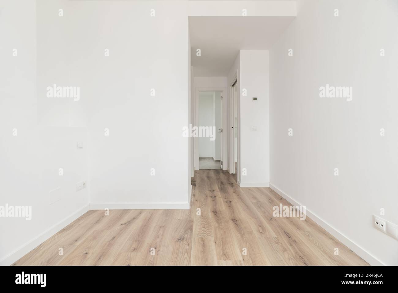 An empty bedroom with an en-suite bathroom in the background, wooden floors and plain white painted walls Stock Photo