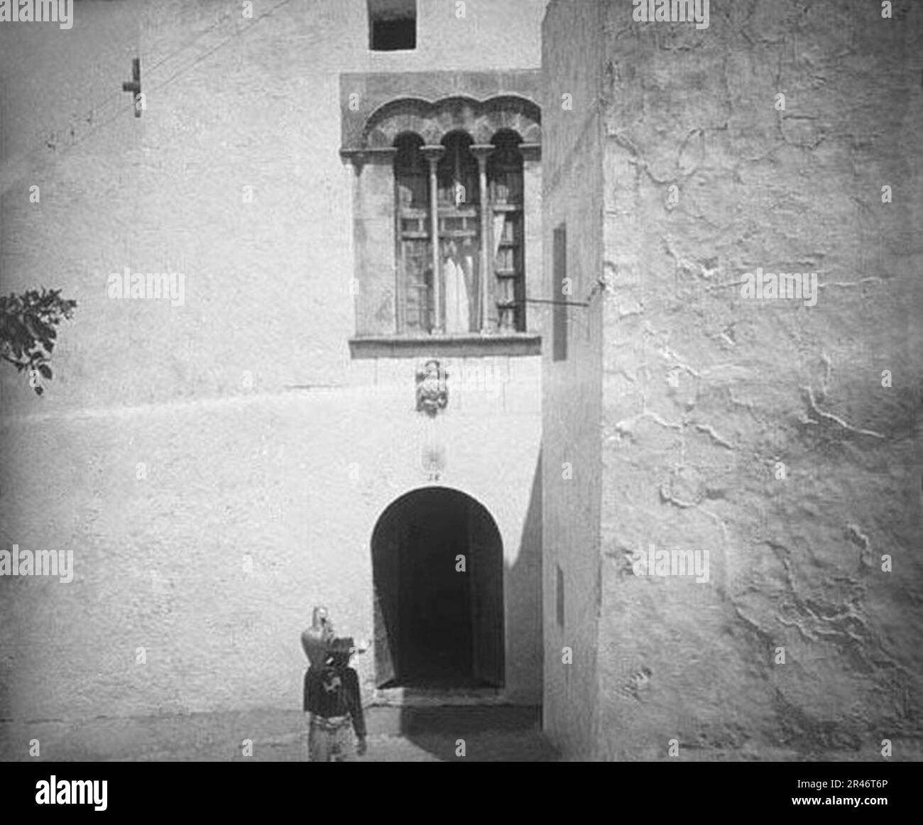 Un home amb un càntir davant de l'antic casal de Can Comasema amb un finestral sobre la porta (Restored) Stock Photo