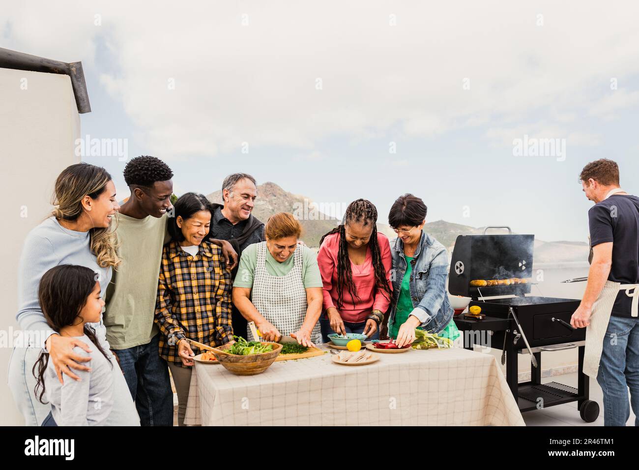 Multigenerational friends having fun doing barbecue at house rooftop - Happy multiracial people cooking together - Summer gatherings and food concept Stock Photo