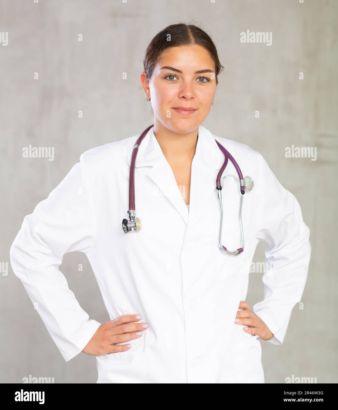 Friendly female professional doctor in white coat posing against gray ...