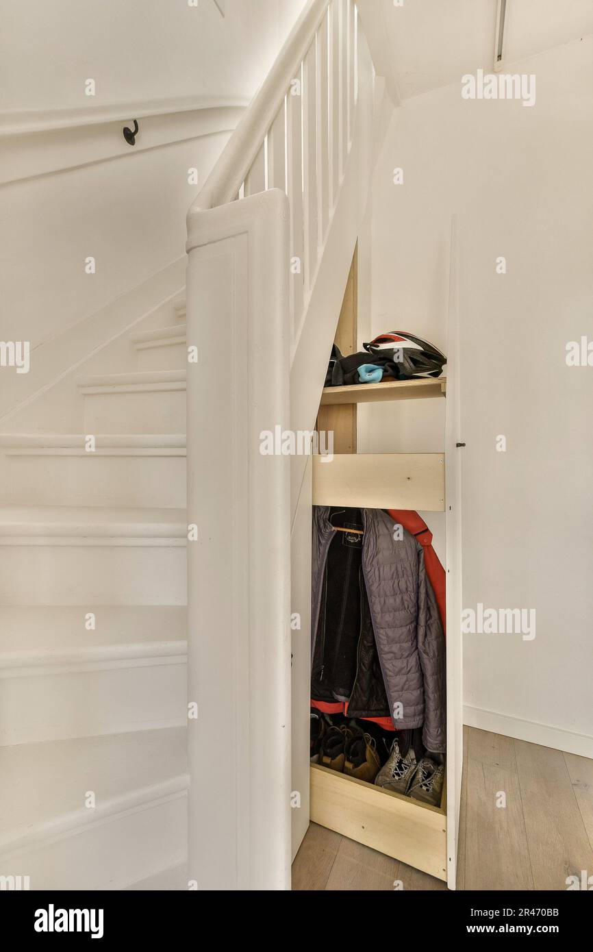 a closet under the stairs in a small room with white walls and wooden flooring there is a coat rack on the wall Stock Photo Alamy