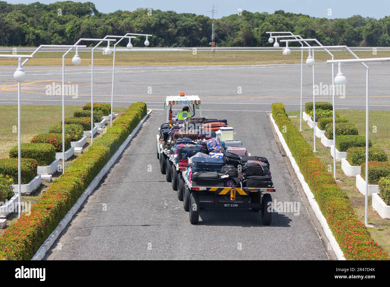 Luggage transport tractor travels from the passenger terminal at Santarem Airport (SBSN) to the aircraft for luggage handling Stock Photo